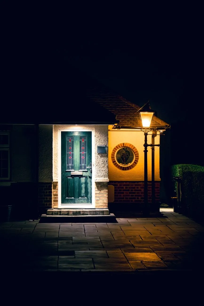 A green composite front door with leaded glass panels lit by a lantern at night