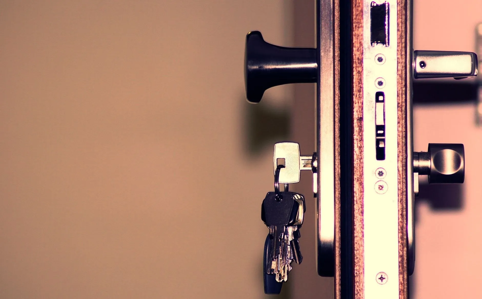 The edge of an open door showing the lock faceplate, latch, bolt and a bunch of keys in the cylinder