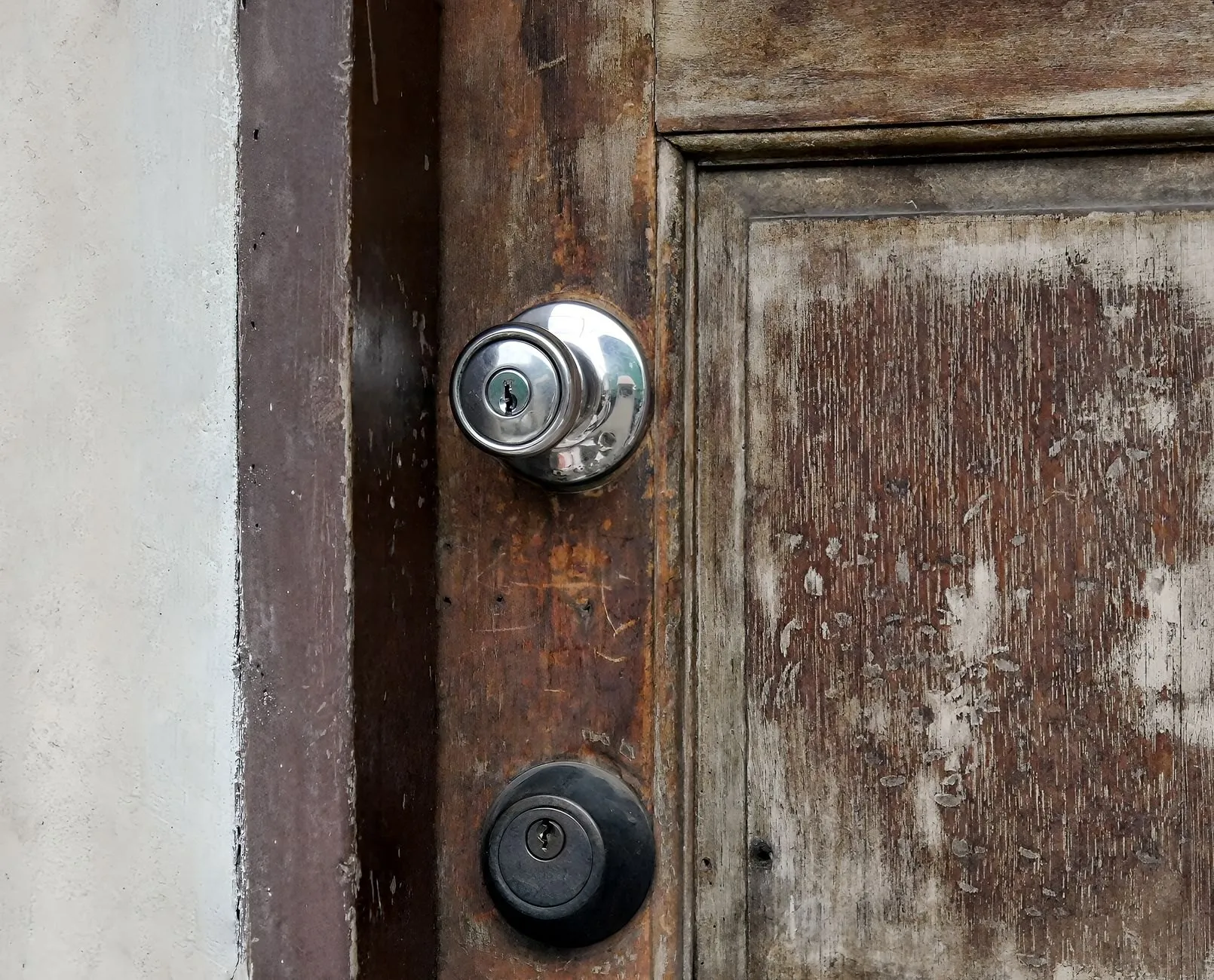 A worn timber door with a knob lock and a deadbolt, paint and wood scuffed around them