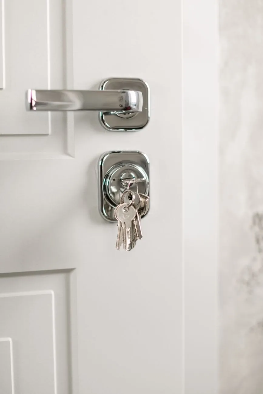 A white front door with a bunch of keys hanging from the cylinder below the handle