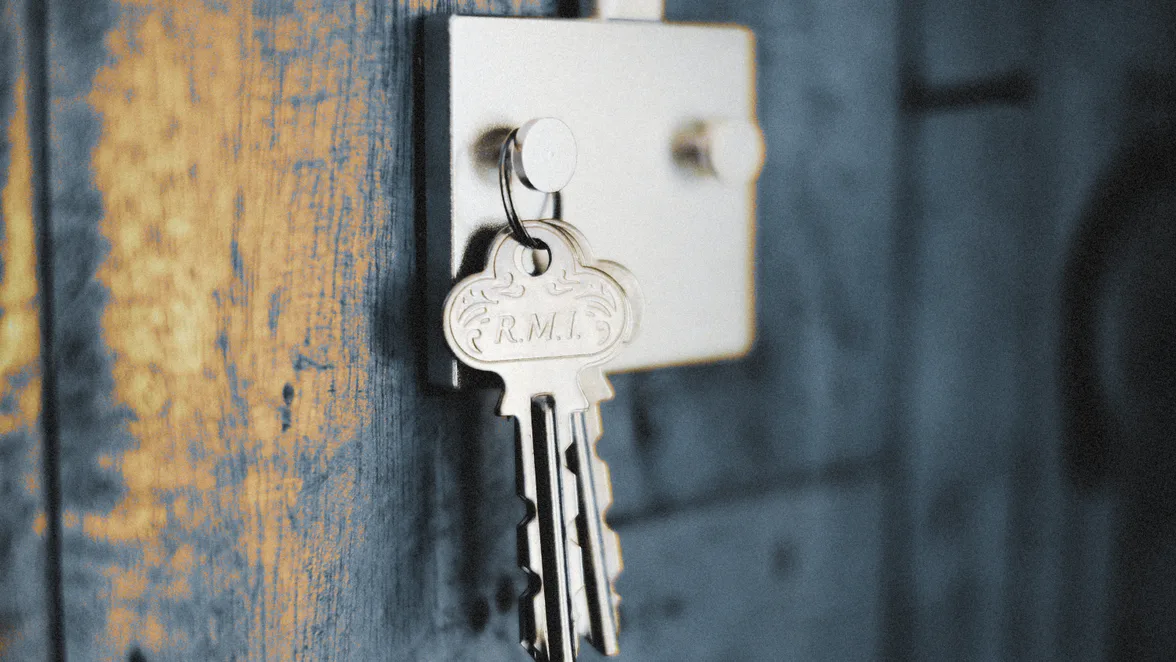 Two keys on a tagged ring left in a rim lock on a painted timber door.